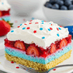 A served slice of Summer Berry Jello Lasagna with whipped cream and sprinkles.